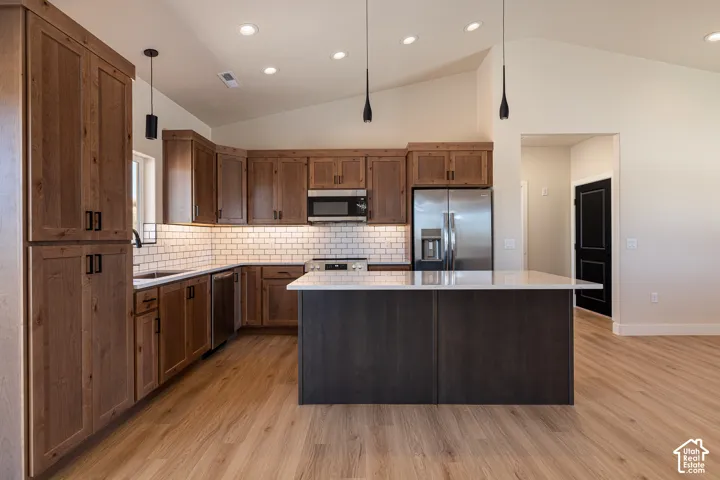 Kitchen featuring wood-finish cabinetry, stainless steel appliances, a white subway tile backsplash, a central island with a light-toned countertop, and recessed lighting