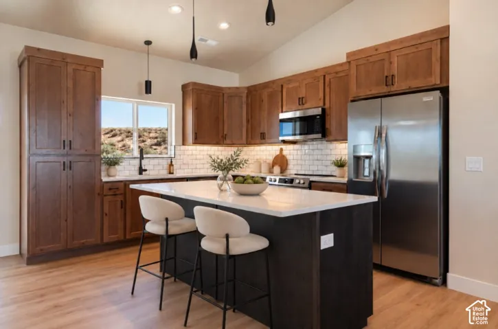 Kitchen featuring wood-finish cabinetry, stainless steel appliances, a white subway tile backsplash, and a central island with a white countertop