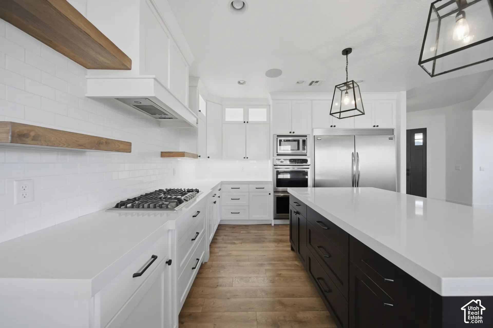 White shaker cabinetry, wood-finish flooring, white subway tile backsplash, stainless steel appliances, and a central island with a white countertop