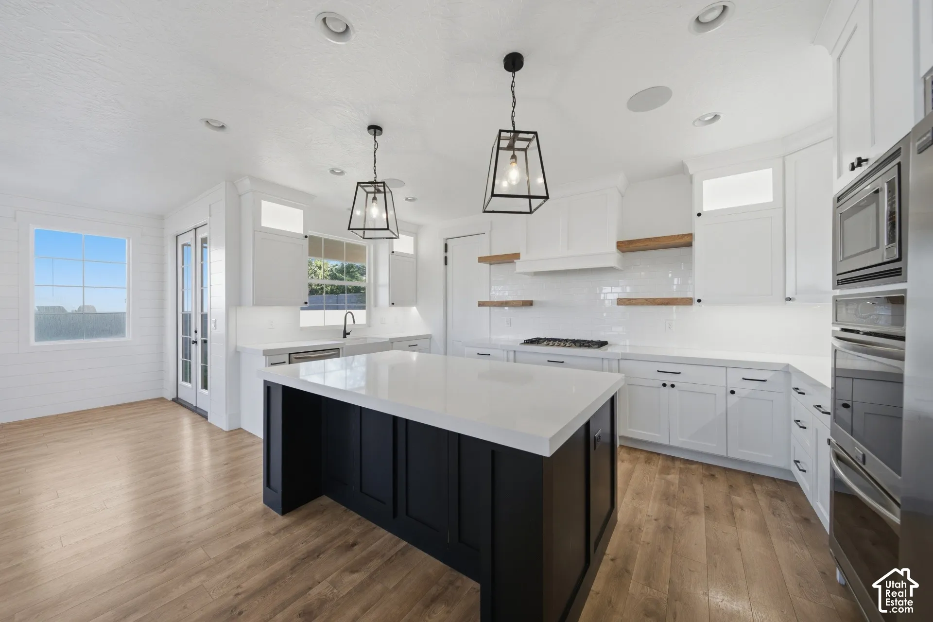 Spacious kitchen featuring a black island with a white countertop, white cabinetry, integrated stainless steel appliances, and wood-finish flooring