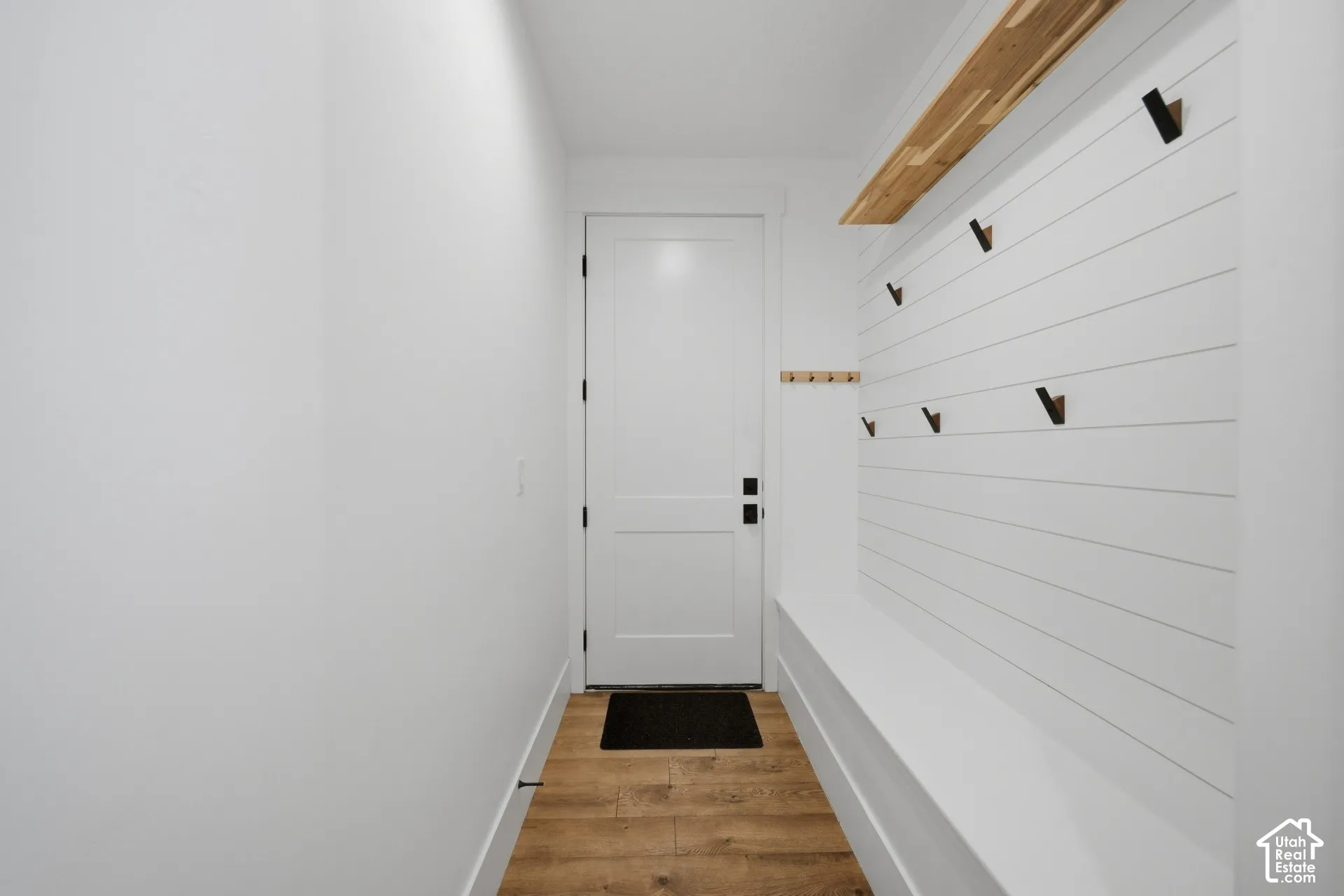 Built-in entryway bench with shiplap wall, wood-finish flooring, and black wall hooks