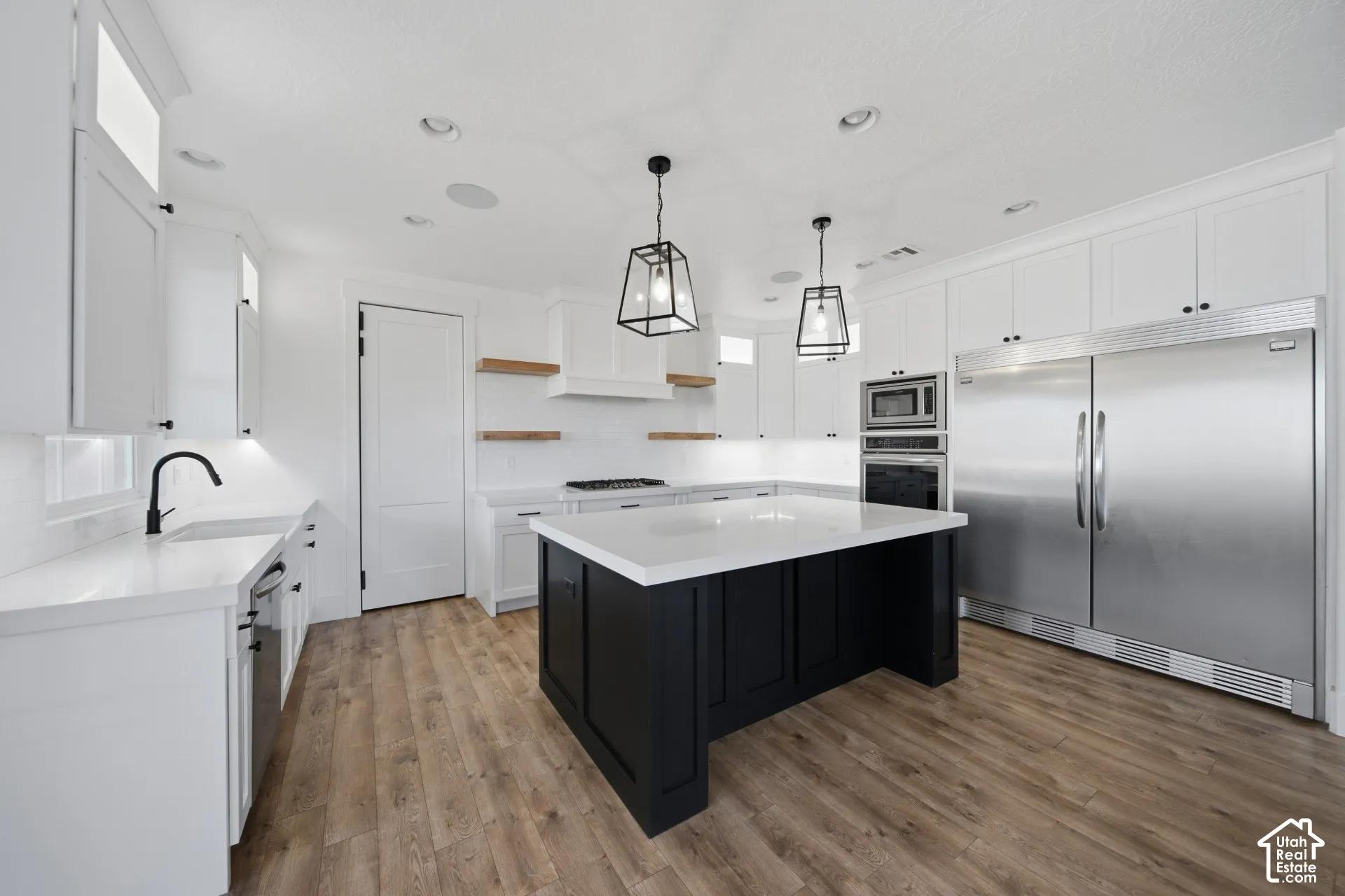 Kitchen featuring white cabinetry, wood-finish flooring, a central island with a white countertop, stainless steel appliances, and matte black light fixtures