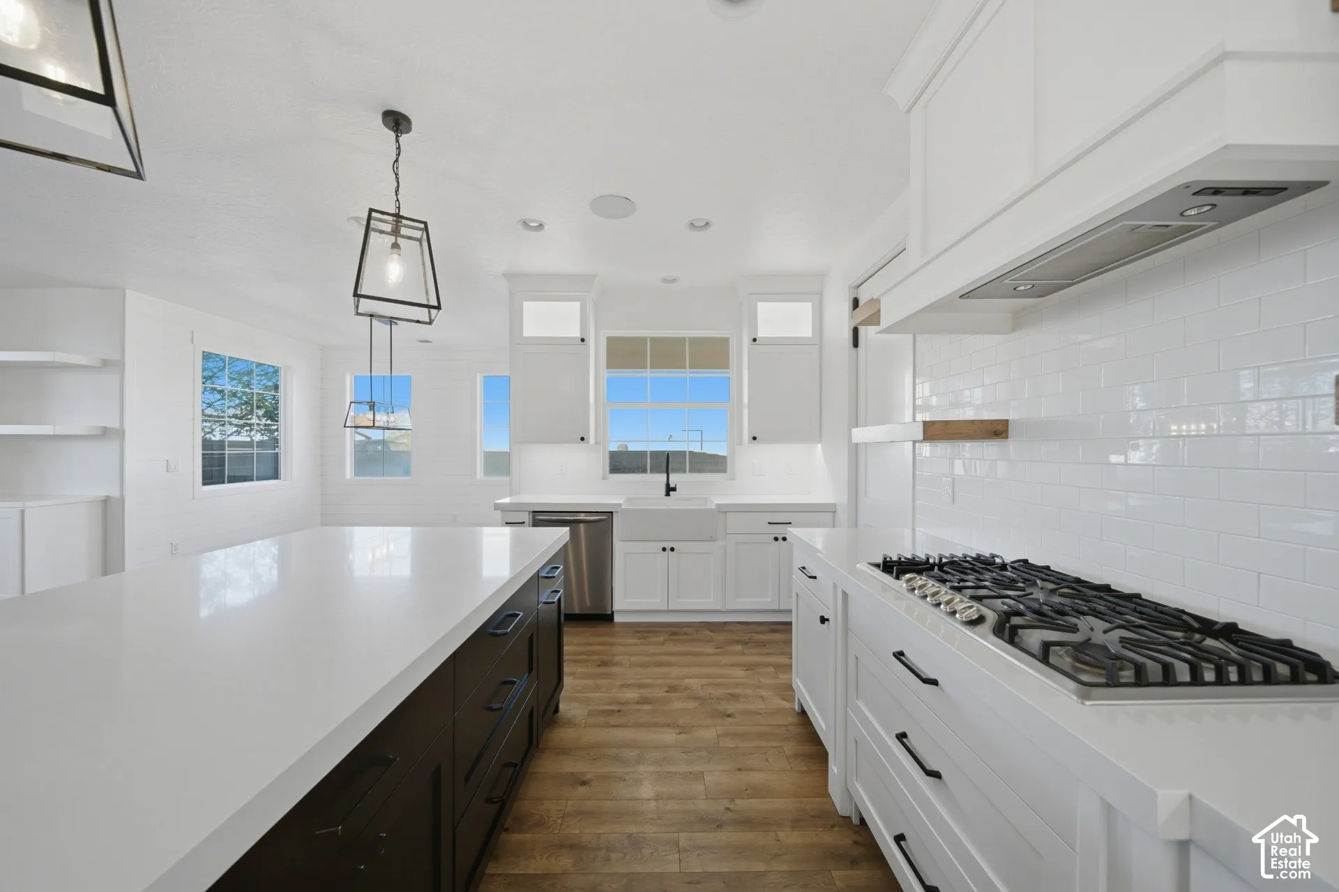 White subway tile backsplash, stainless steel gas range, white shaker cabinetry, large center island with dark base, and wood-finish flooring