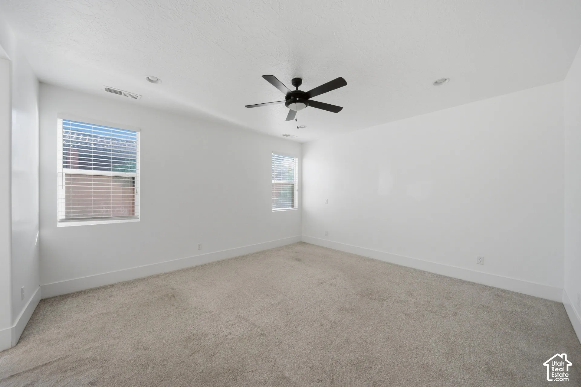 Spacious room featuring neutral carpeting, two large windows with blinds, a ceiling fan, and recessed lighting