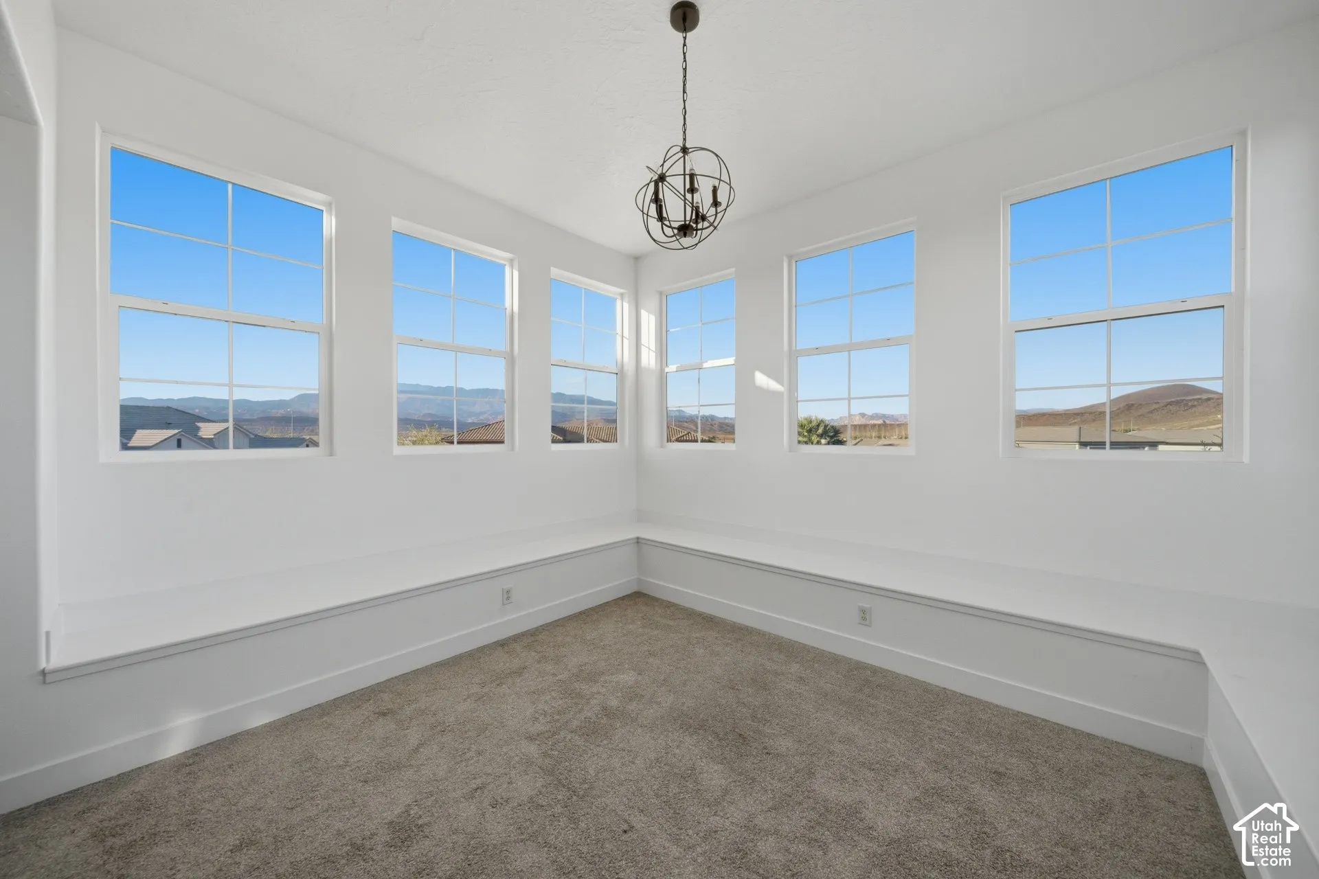 Multiple large windows, neutral-toned carpeting, built-in bench seating, and a decorative ceiling light fixture