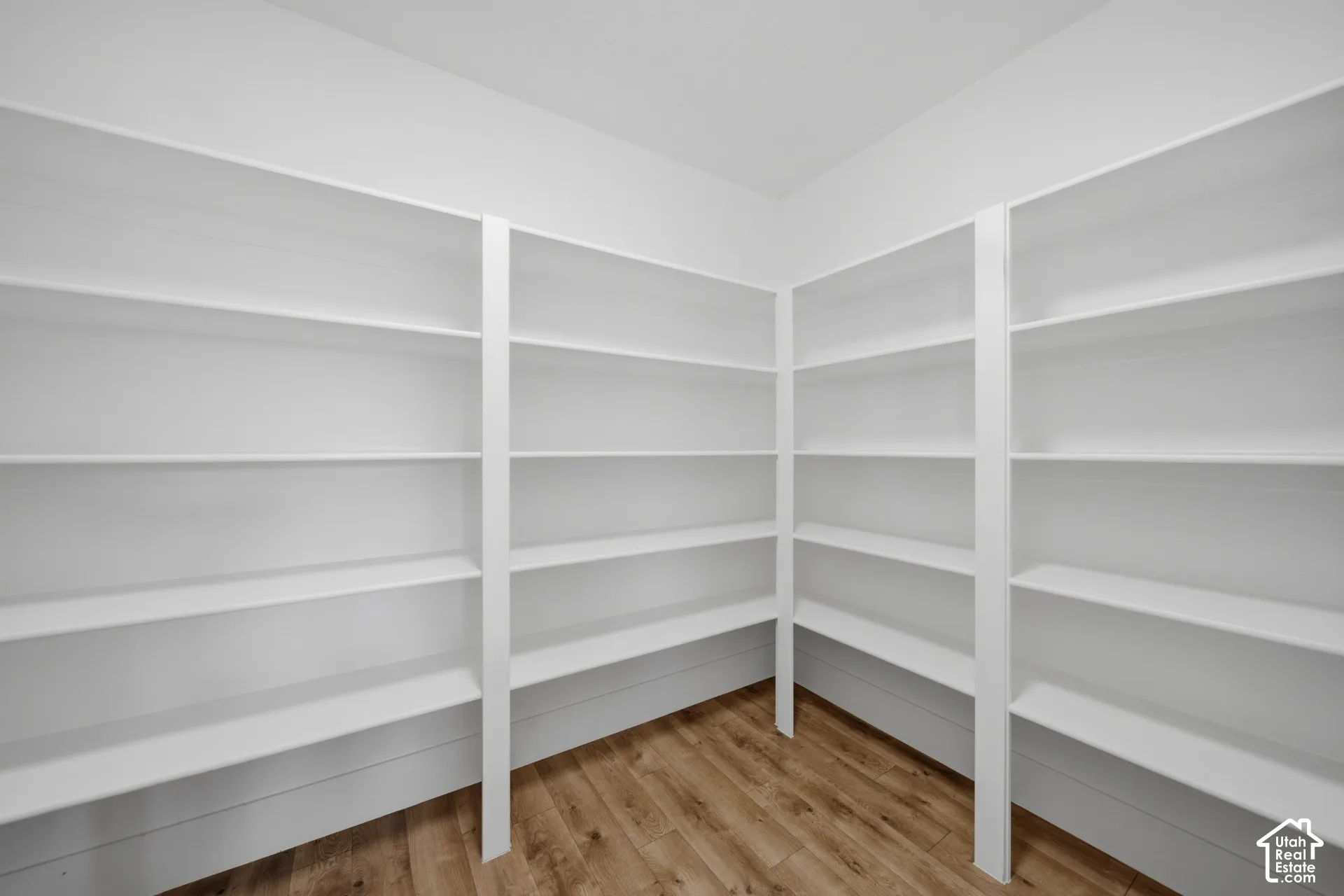 Expansive corner pantry featuring multiple rows of built-in white shelving and wood-finish flooring