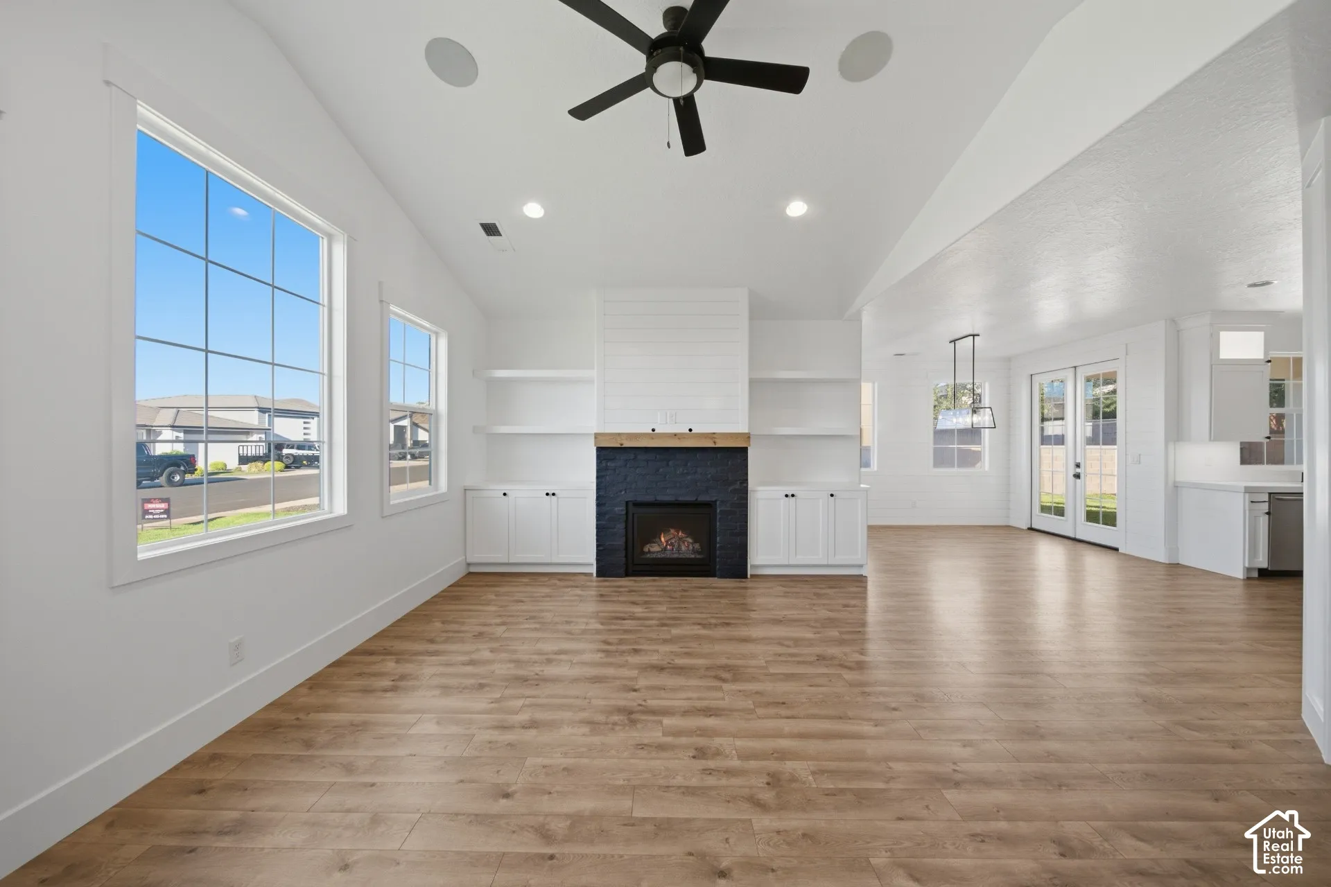 Vaulted ceiling, wood-finish flooring, built-in fireplace with dark tile surround, built-in shelving, and large windows