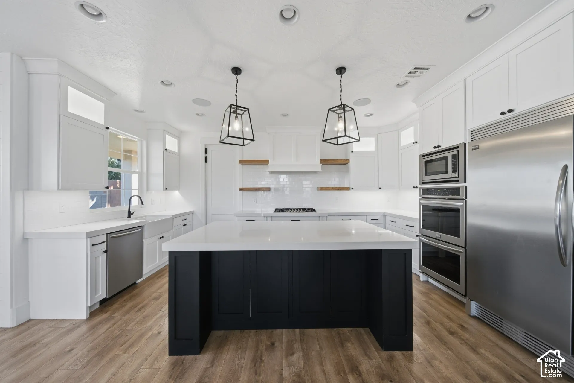 Contemporary kitchen featuring a black island with a white countertop, white cabinetry, stainless steel appliances, and wood-finish flooring