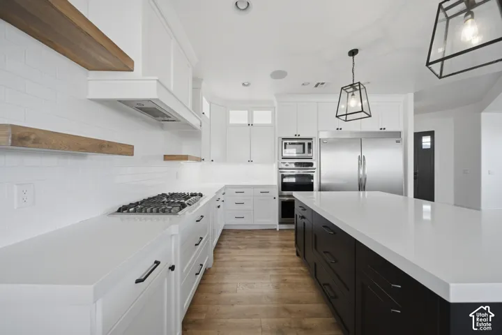 White shaker cabinetry, wood-finish flooring, white subway tile backsplash, stainless steel appliances, and a central island with a white countertop