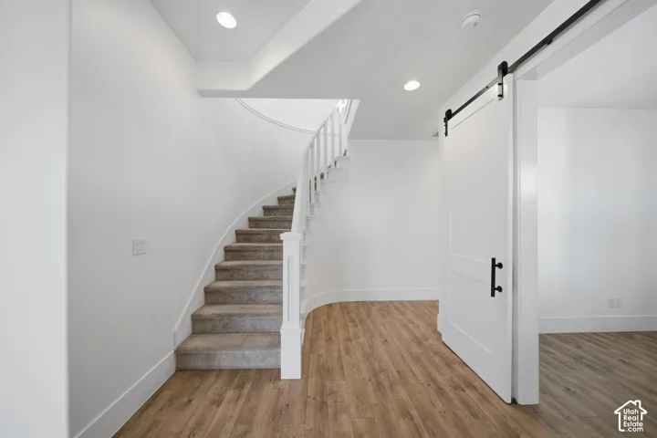 Curved staircase with carpeted treads, wood-finish flooring, white walls, recessed lighting, and a white barn door with black hardware