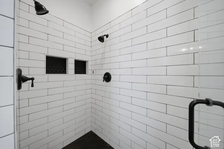 Shower with white subway tile, black hexagon tile flooring, dual shower heads, recessed shelving, and a clear glass enclosure