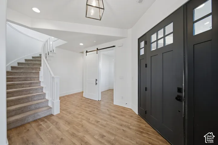 Double entry doors with glass panels, wood-finish flooring, a curved staircase with white railings, and a white barn door