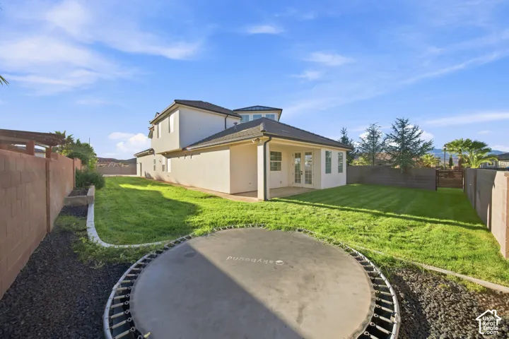 Expansive backyard featuring a manicured lawn, established landscaping, and a patio area with double glass doors