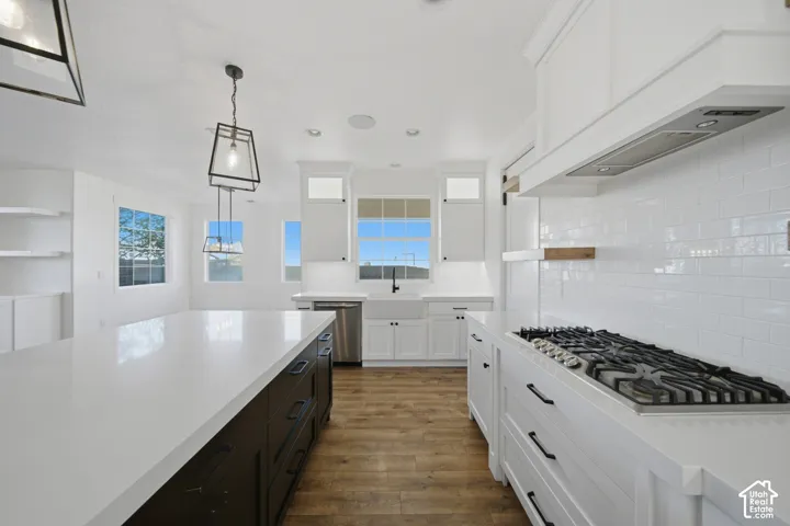 White subway tile backsplash, stainless steel gas range, white shaker cabinetry, large center island with dark base, and wood-finish flooring