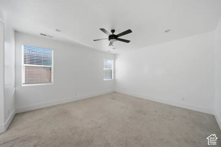 Spacious room featuring neutral carpeting, two large windows with blinds, a ceiling fan, and recessed lighting