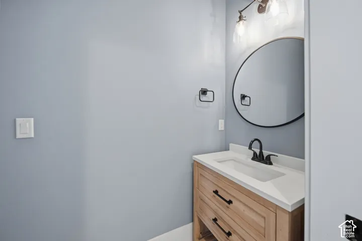Wood-finish vanity with drawer storage, white countertop with integrated sink, matte black faucet, round wall-mounted mirror, and wall-mounted light fixture