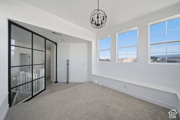 Carpeted room featuring a spherical chandelier, three large windows, a window bench, and a pivoting glass panel wall with black framing