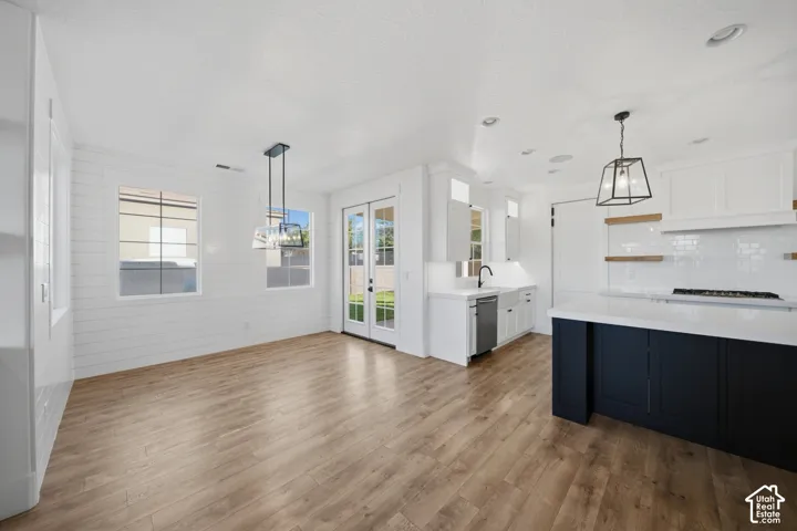 Open-concept living space with wood-finish flooring, white shiplap walls, pendant lighting, and a kitchen featuring white cabinetry, a dark island, and a tile backsplash