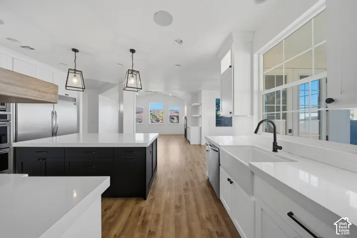 Spacious kitchen featuring two islands, white countertops, built-in stainless steel appliances, wood-finish flooring, and white cabinetry with black hardware