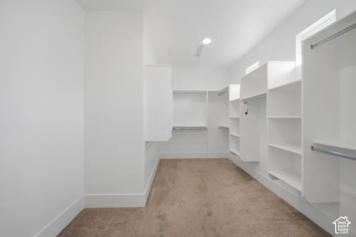 Expansive closet featuring built-in white shelving, integrated hanging rods, recessed lighting, and soft carpet flooring