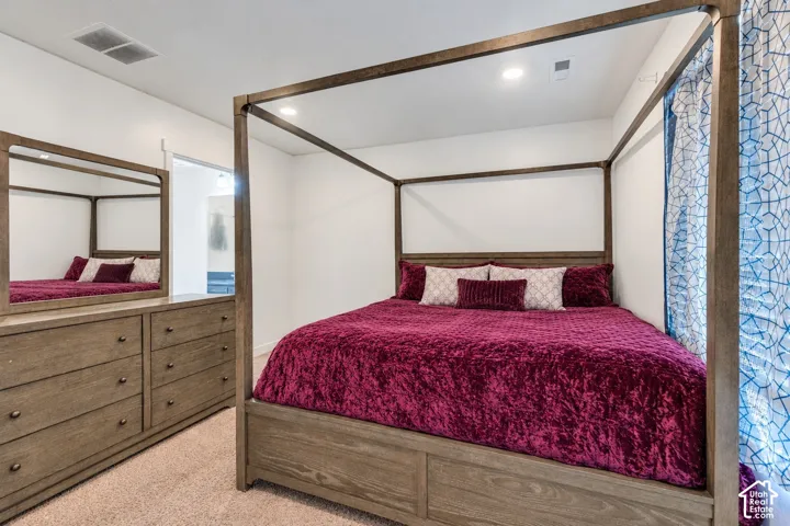 Recessed lighting illuminates this room featuring light-colored carpeting, a built-in dresser with a mirror, and white walls