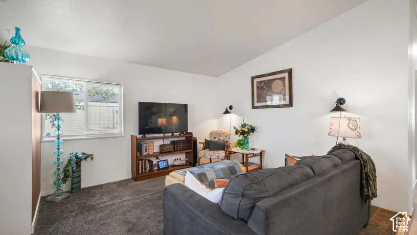 Vaulted ceiling, wall-mounted light fixtures, built-in bookshelf, and a window with blinds