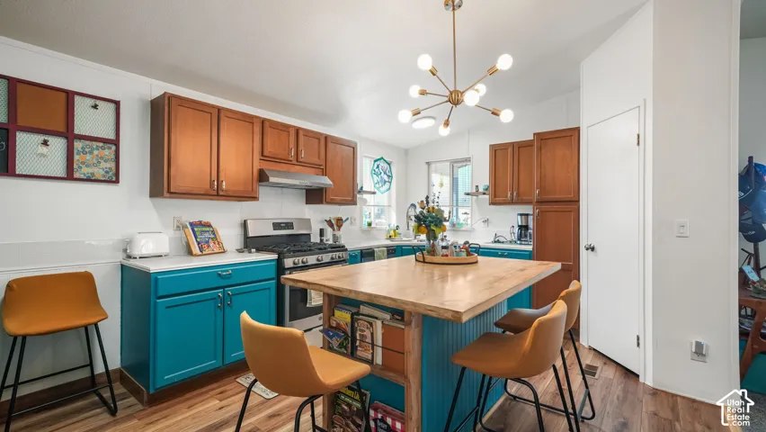 Kitchen featuring wood-finish flooring, a central island with a wood-finish countertop, stainless steel appliances, and a modern Sputnik-style chandelier