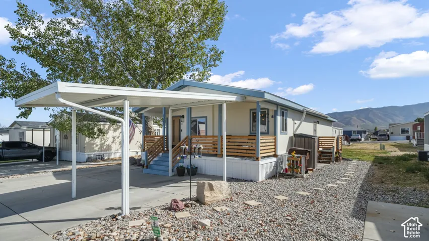 Carport structure, front porch with wood railing, gravel landscaping, exterior siding, and mountain backdrop