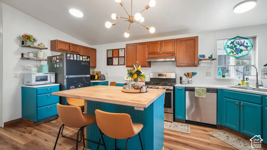Wood-finish flooring with a kitchen island featuring a wood-tone countertop, teal cabinetry, and stainless steel appliances