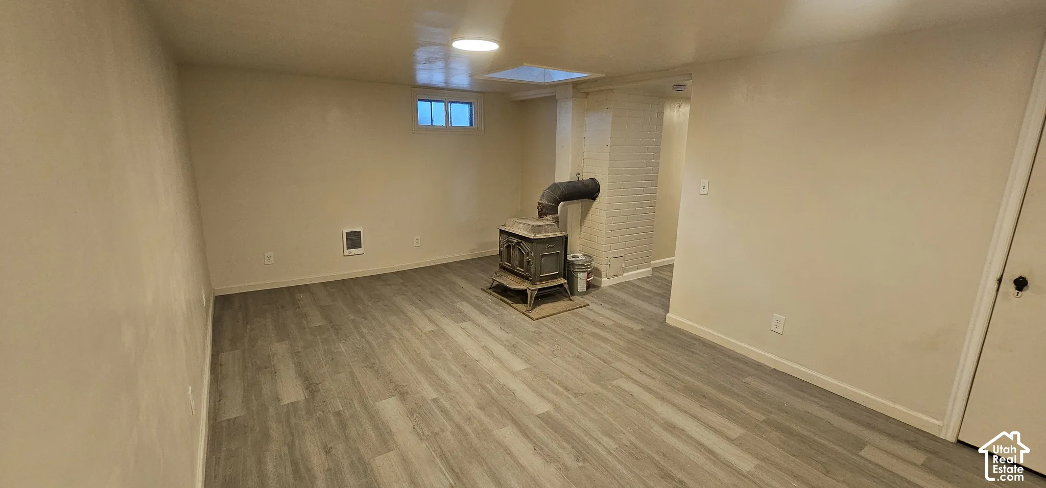 Recessed lighting, wood-finish flooring, white brick accent, window, and a built-in wood-burning stove