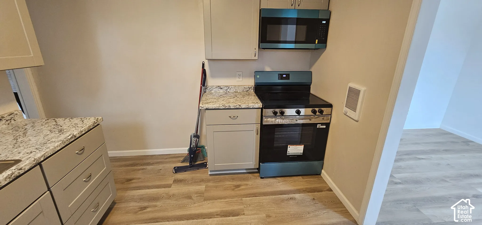 Contemporary kitchen featuring light wood-finish flooring, light-toned cabinetry, granite-style countertops, and a full-size range with an overhead microwave