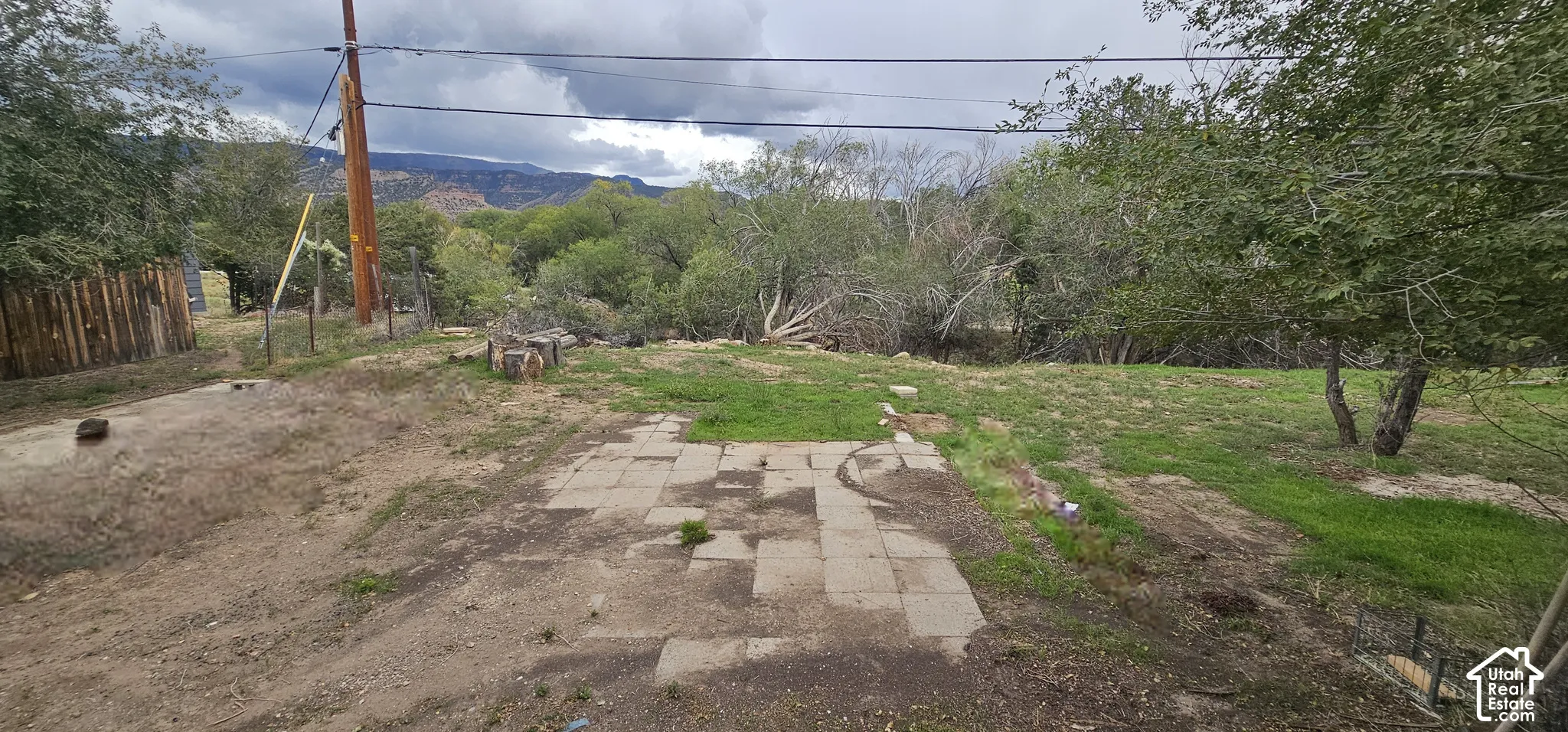 Paved patio area opening to a sloped lot with mature trees and mountain scenery