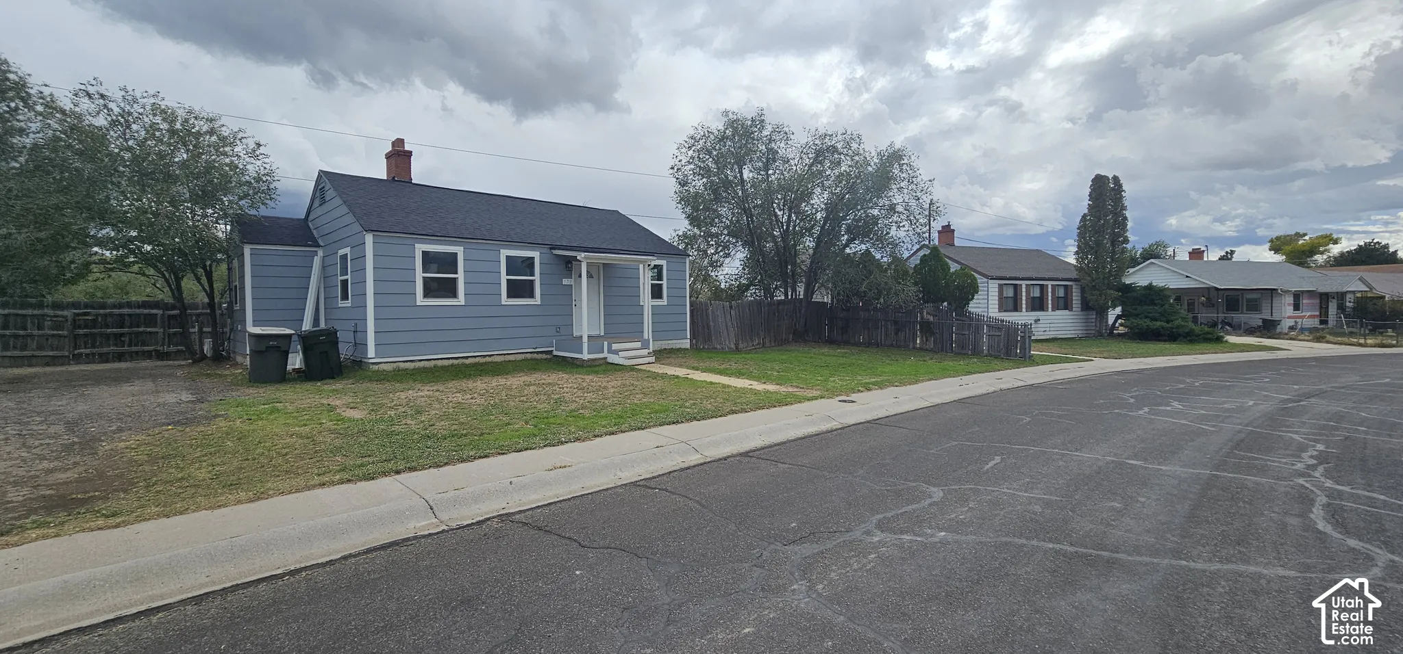 Light blue exterior siding, white trim windows, dark shingle roofing, and a brick chimney
