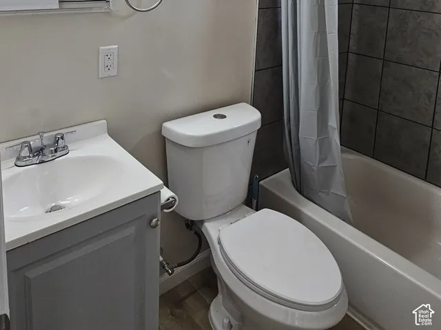 Bathroom featuring a shower-tub combination with dark tile surround, a single-basin vanity with a gray cabinet, wood-finish flooring, and a mirrored medicine cabinet