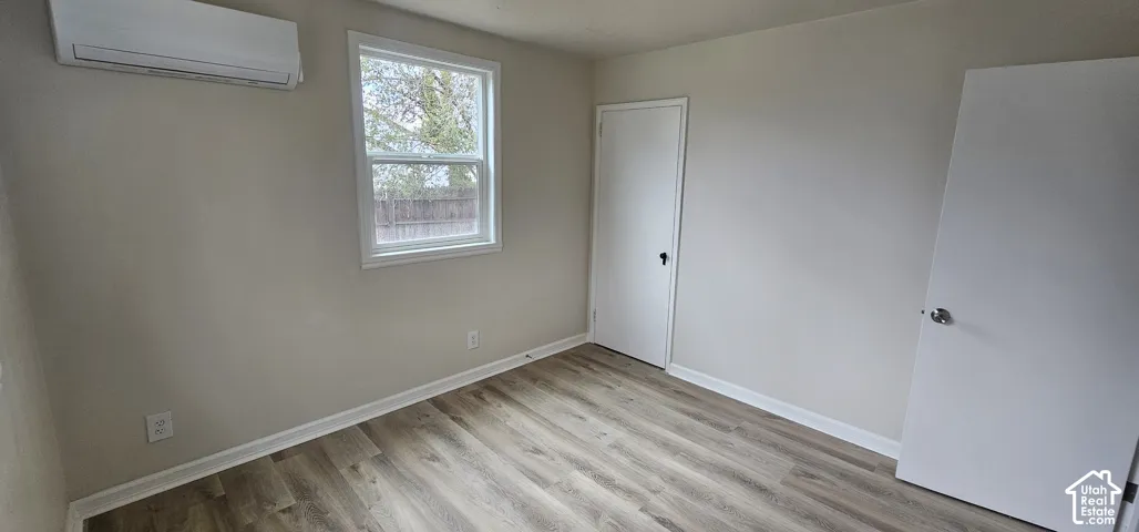 Wood-finish flooring, white trim, rectangular window, built-in air conditioning unit, and white interior doors