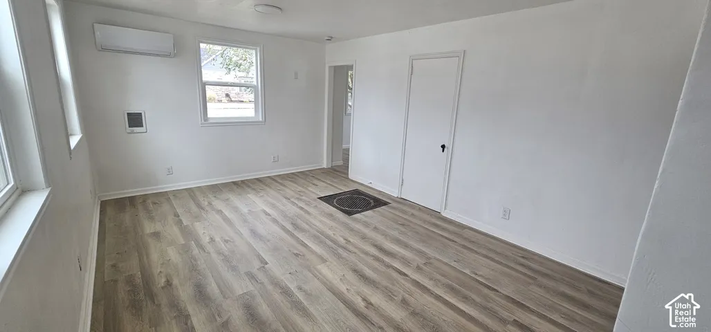 Wood-finish flooring, white walls, and a wall-mounted climate control unit