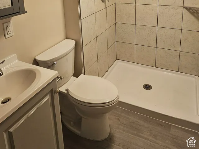 Wood-finish flooring with a vanity, toilet, and tiled shower