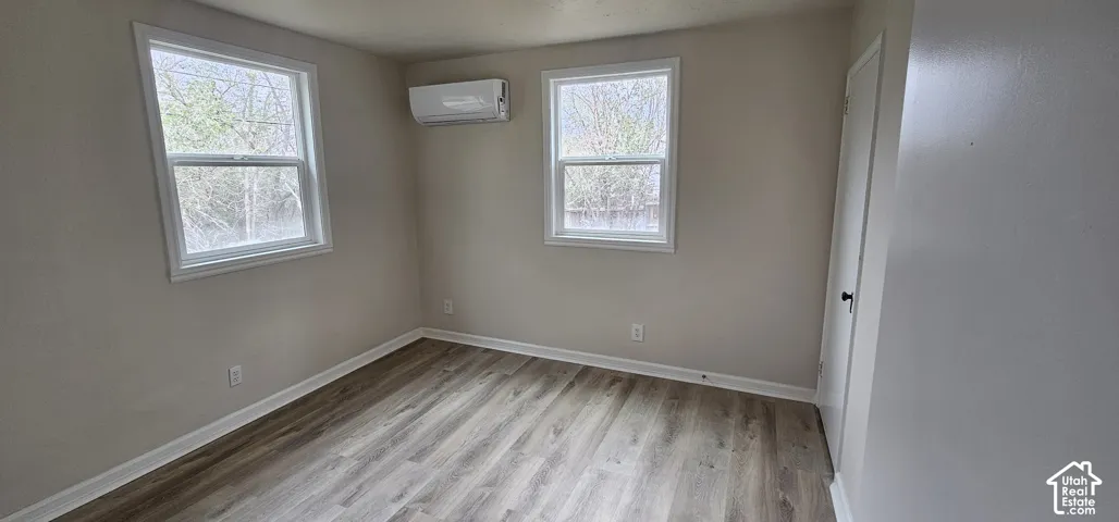 Light-toned wood-finish flooring, two large windows with white trim, and a wall-mounted air conditioning unit