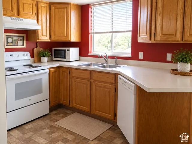 Kitchen featuring wood cabinetry, white appliances, dual basin sink, and a large window