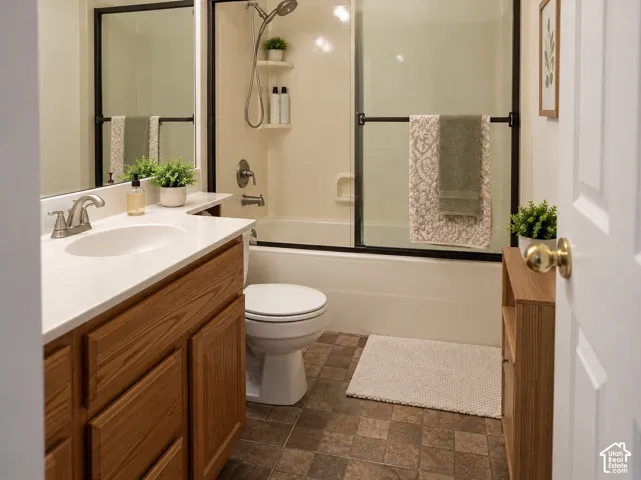Bathroom featuring a shower-tub combination with sliding glass doors, a vanity with a white countertop and wood-finish cabinetry, and a toilet