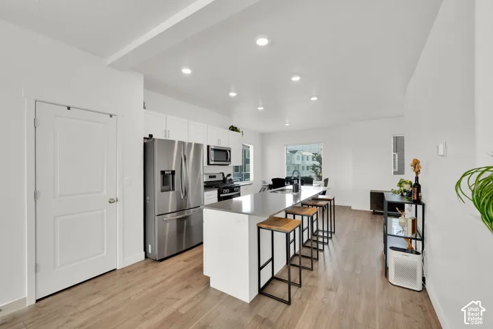 Open-concept kitchen featuring stainless steel appliances, a large island with seating, white cabinetry, and wood-finish flooring