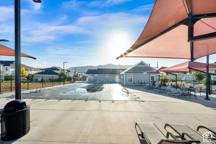 Concrete pool deck with shade structures, a fenced swimming pool, and a building with gray siding