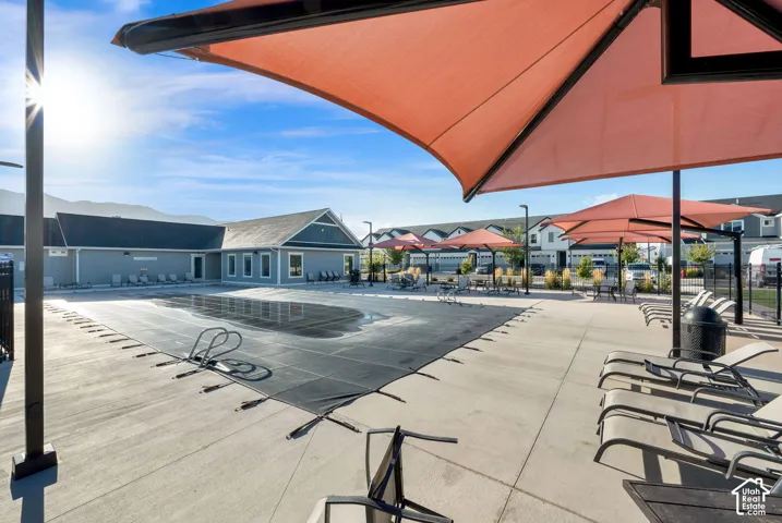 Outdoor recreation area featuring a covered pool, concrete pool deck, shade structures, and a single-story building with multiple windows