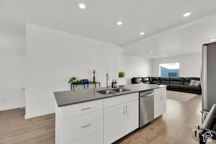 Kitchen island with dual stainless steel sink, stainless steel dishwasher, white cabinetry, and a dark-toned countertop