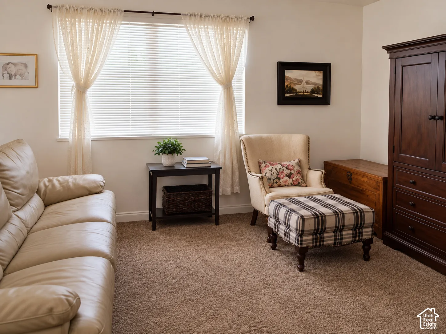 Neutral wall color, window with blinds, carpeted flooring, dark wood side table, wood trim accents