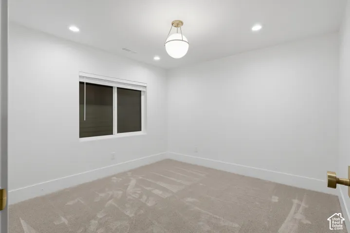 Recessed ceiling lighting, a contemporary pendant light fixture, window with blinds, and light-toned carpeting