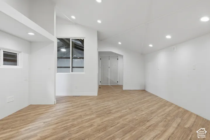 Wood-finish flooring, recessed lighting, vaulted ceiling, white walls, and a multi-pane window