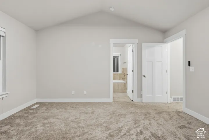 Vaulted ceiling, neutral tone carpeting, white interior doors, and a window with white trim