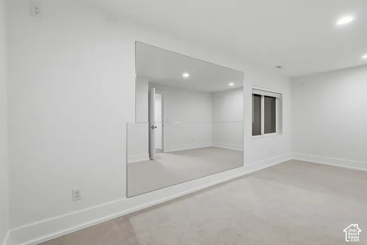 Wall-to-wall carpeting, expansive wall mirror, window with roller shade, and recessed lighting