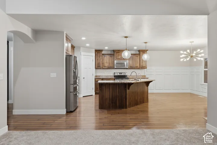 Kitchen with wood-finish flooring, wood cabinetry, stainless steel appliances, and a central island with a sink